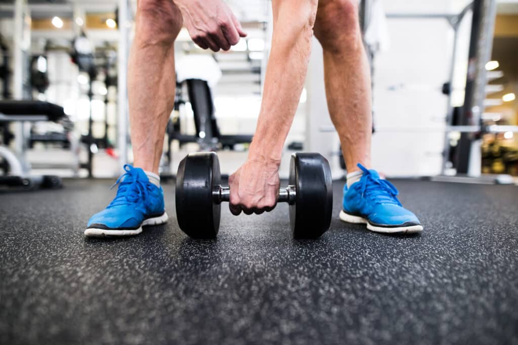 Image of a senior man preparing to lift a heavy dumbbell off the ground