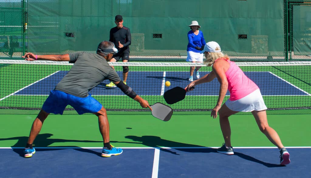 Pickleball injuries can happen from lack of preparation. in this image four active seniors play pickleball together