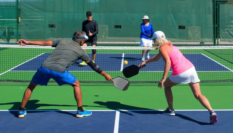 Pickleball injuries can happen from lack of preparation. in this image four active seniors play pickleball together