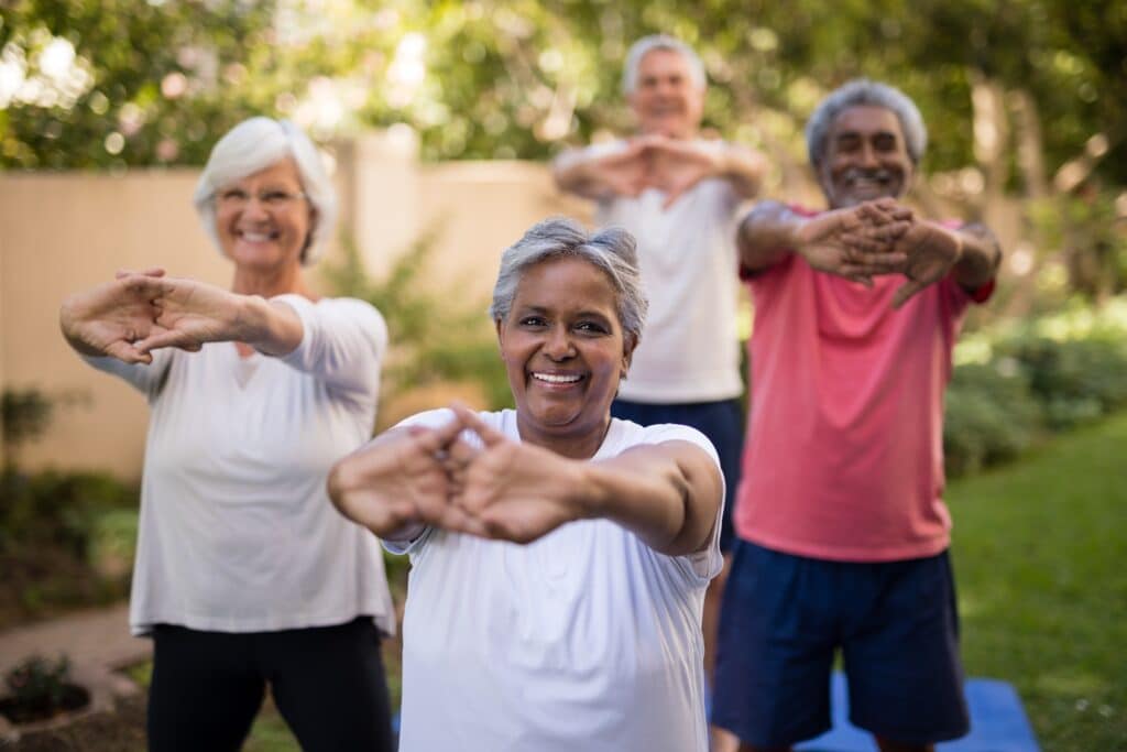 Image of senior friends stretching their hands and wrists outdoors as self-care practice for rheumatoid arthritis