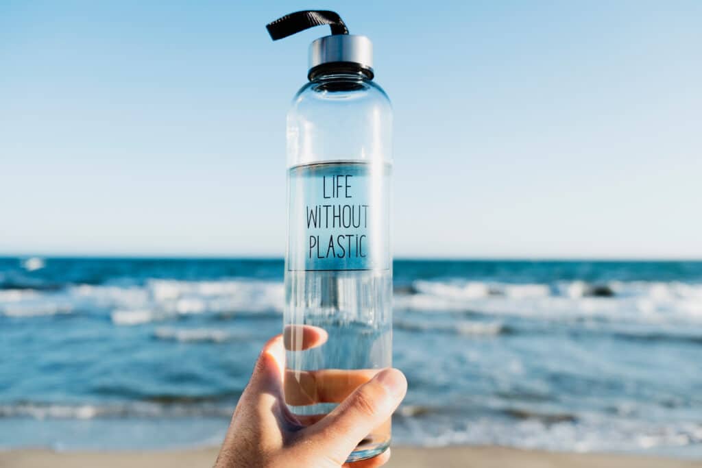 Plastics in the body: a person holds a glass water bottle at the beach