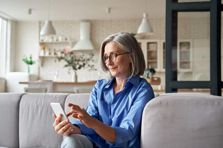 How to make a physical therapy appointment: a senior woman looks at her iphone in her living room