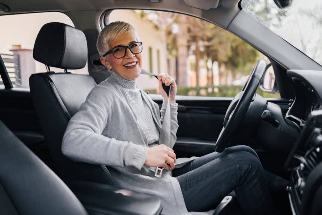 Image of a smiling senior woman seated in the driver's seat of her car.