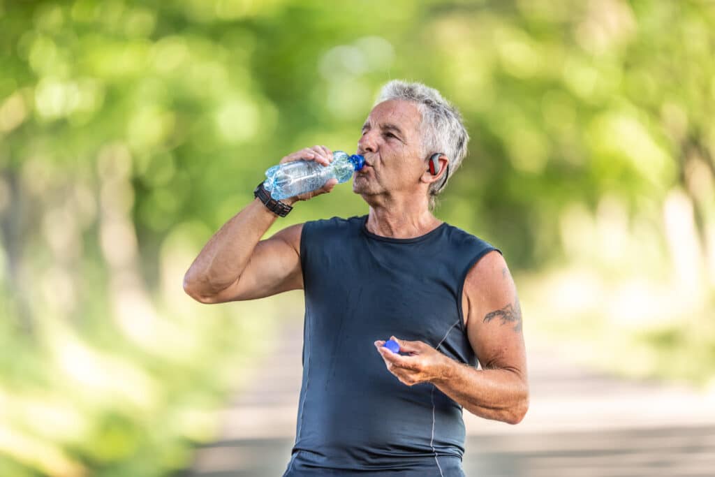 Plastics in the body: a senior man drinks from a plastic water bottle on a run.