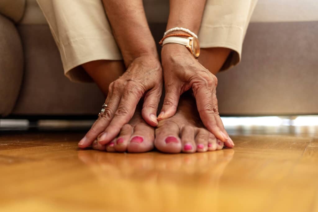 Image of a senior woman rubbing her sore feet.  Senior toenail care is paramount to healthy feet as we get older.