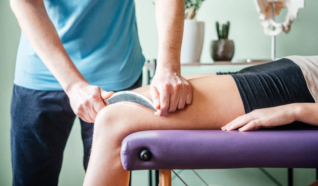 A patient receives IASTM treatment on her quadriceps muscles
