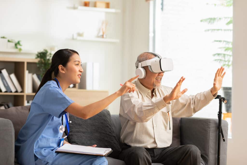 Telerehabilitation in Physical Therapy: a senior man tries virtual reality with the help of a nurse.