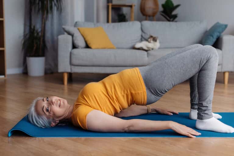 Hip extension involves engagement of the gluteal muscles to drive the hips forward as in this image of a senior woman doing a bridge exercise.