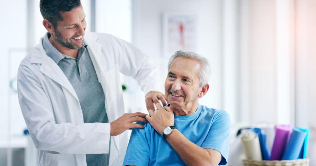 Smiling doctor examines a patient with a shoulder pain to screen for shoulder replacement.
