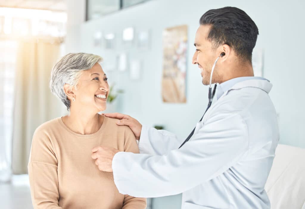 Image of a woman getting a heart examination from her doctor. Physical therapy's role in coronary artery disease includes following up with a patient's doctor