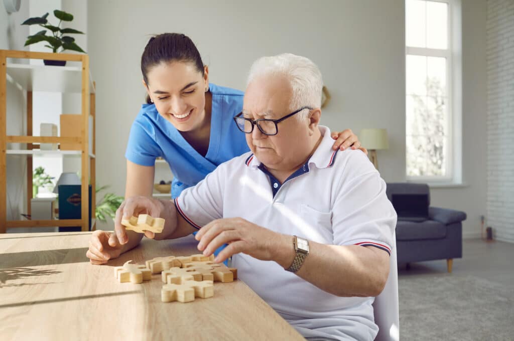 Image of a smiling nurse assisting a senior man with dementia exercises.