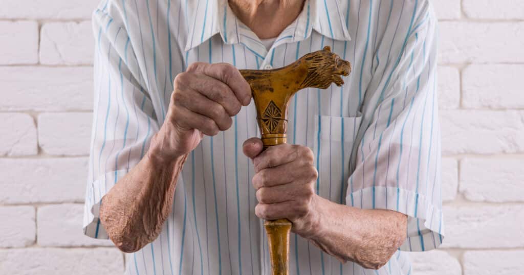 A Guide to Body Mechanics for Better Balance: Image of a frail older man holding a carved wooden cane. 