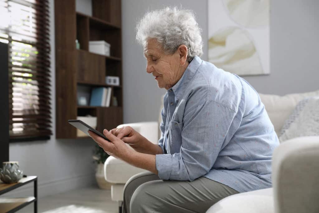 Image of an older woman sitting slumped over her ipad on a couch, encouraging bad posture