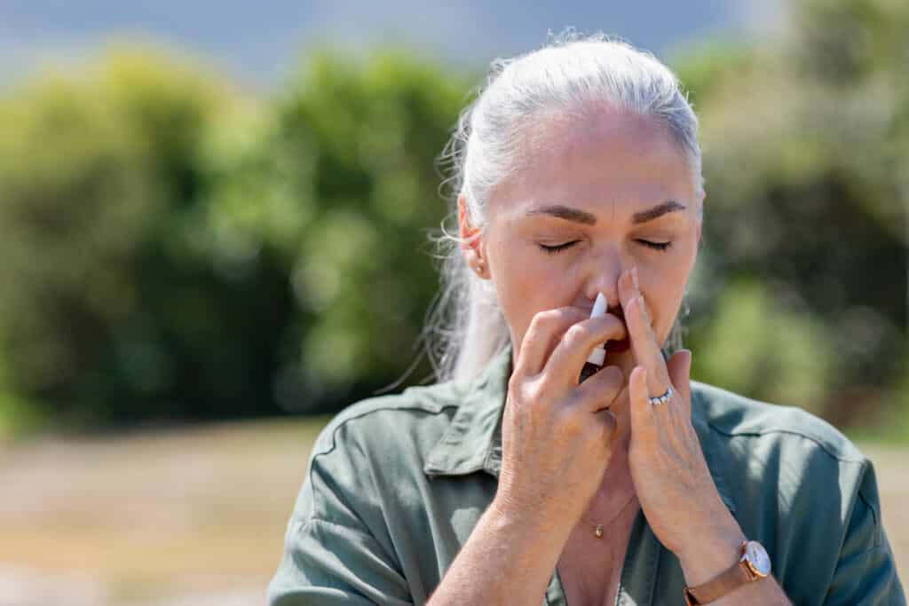 Image of an older woman using a nasal spray to prevent sneezing injuries.
