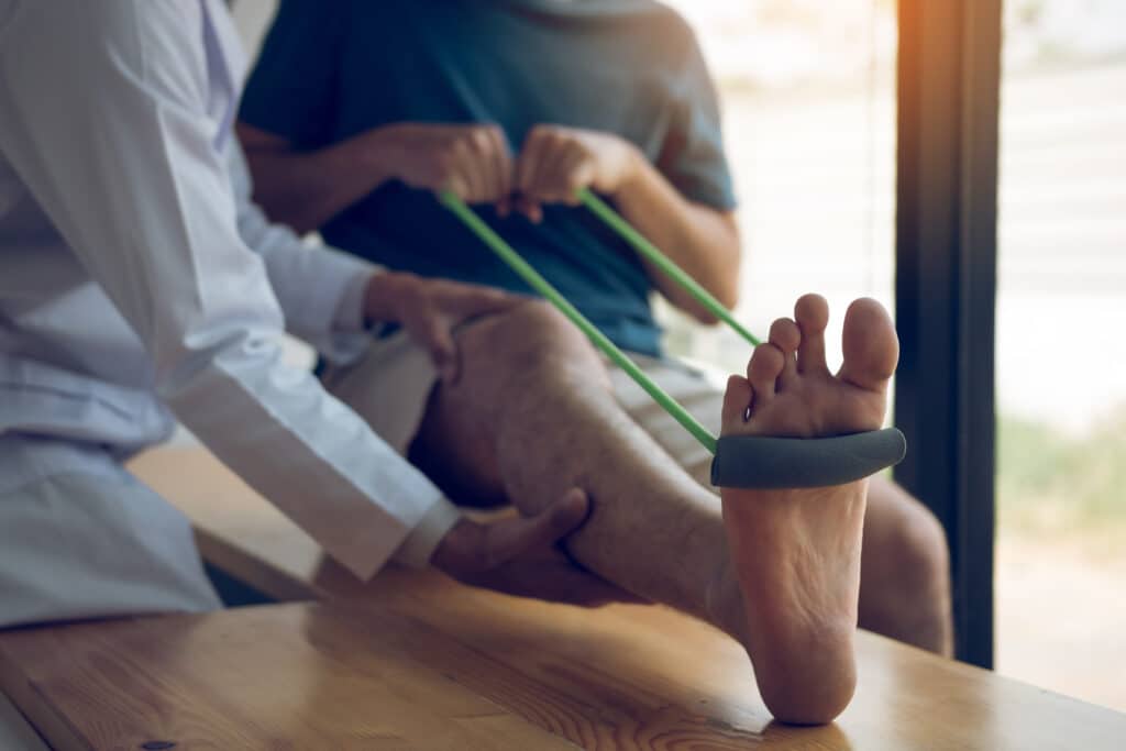 Image of a physical therapist assisting a patient with foot and calf exercises with an exercise band.