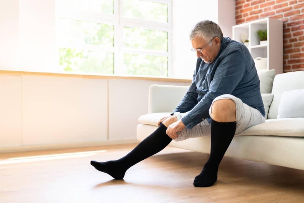 Exercises to Get Rid of Swelling in Ankles and Feet: Image of man rolling a compression stocking over swollen foot. 
