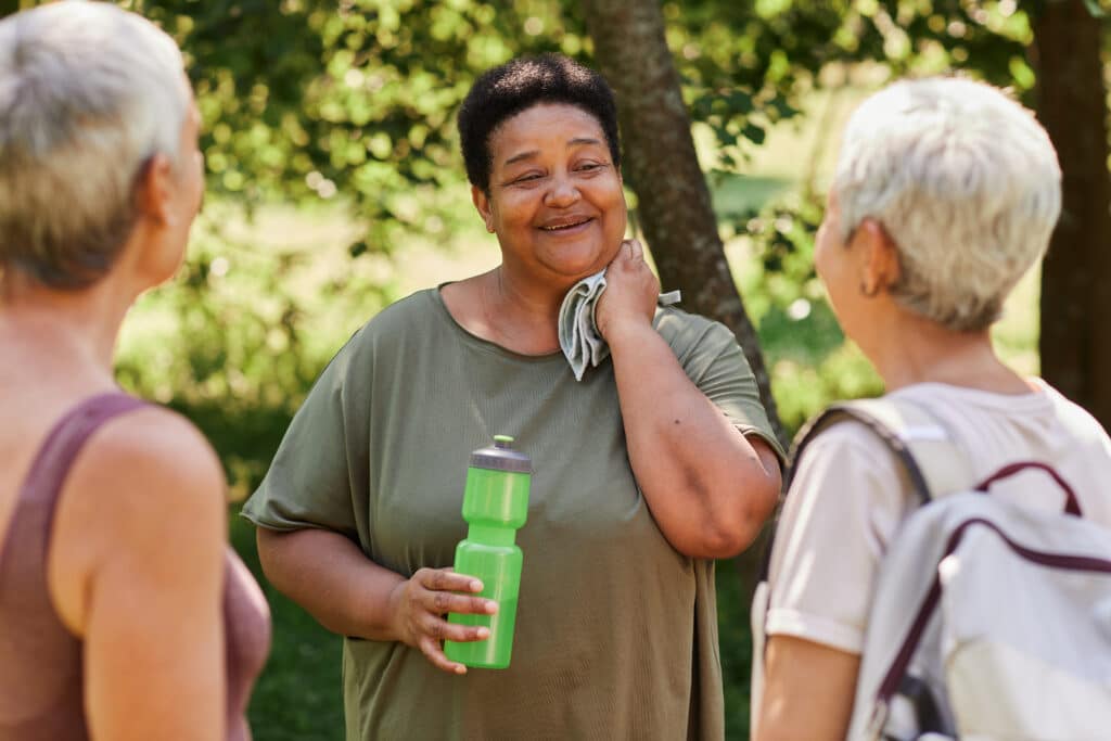 How To Tell If You Are Out of Shape & What to Do About It: Portrait of overweight senior woman chatting with friends after an outdoor workout in park and smiling happily