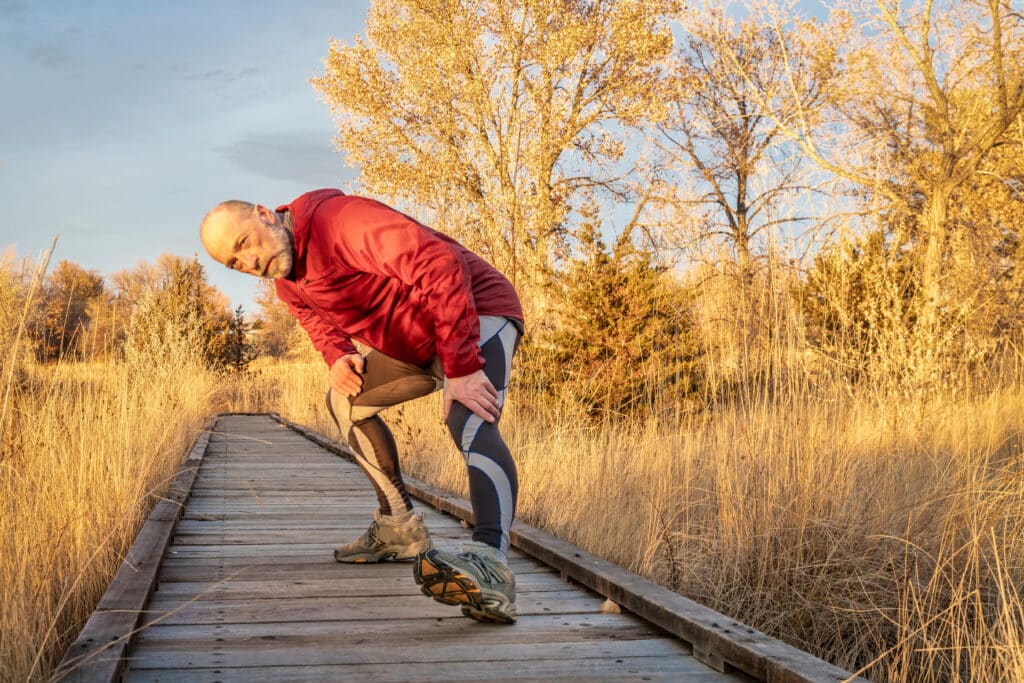 The Best Walking Stretches for Walking: Image of an older senior man stretching his hips and legs outdoors 