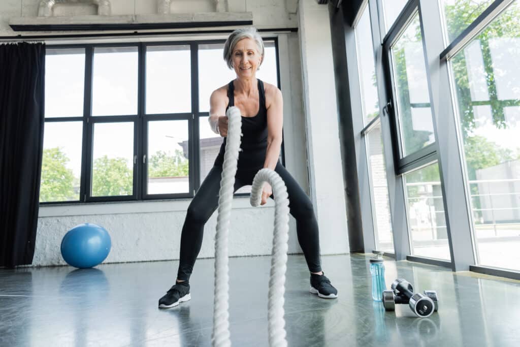 Image of an older woman using battle ropes at the gym.  HIIT training exercise can improve cognitive function for people of all ages