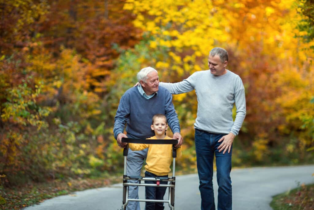 Image of older man with dementia walking in the fall leaves with his son and grandson