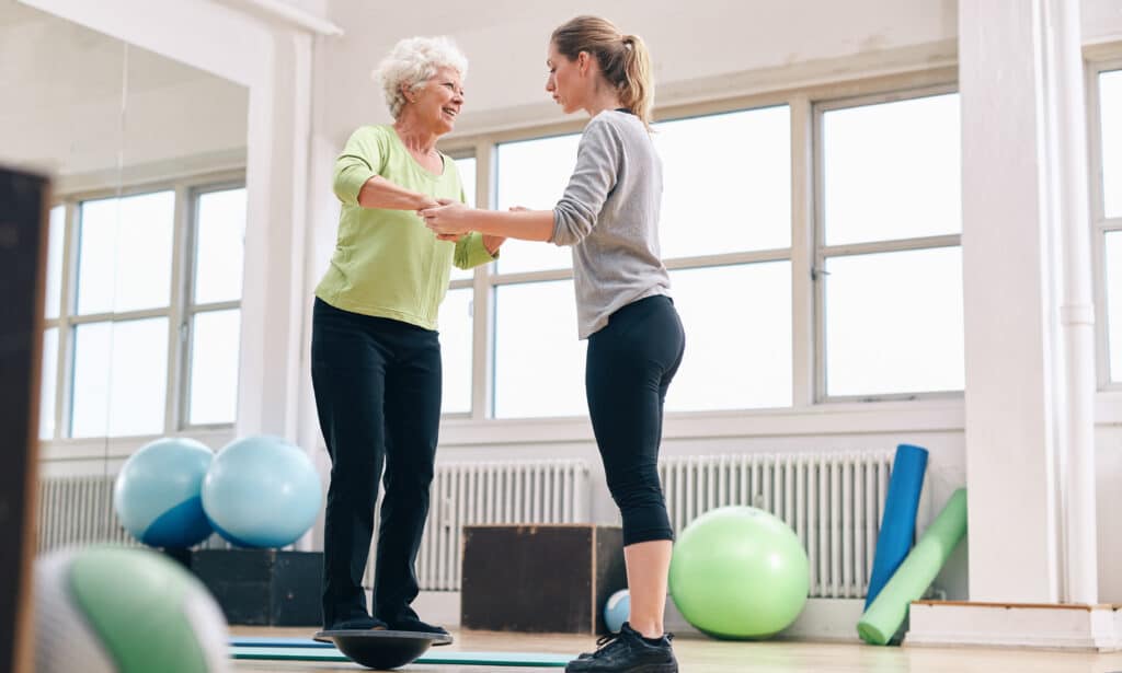Woman balancing on unstable surface balance disc with physical therapist