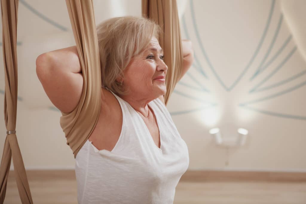 How to decompress spine at home — Image of an older woman using a yoga hammock for neck and back stretches for spinal decompression. 