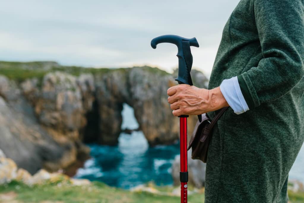 Image of a senior holding a walking pole-cane hybrid outdoors at a cliff's edge.