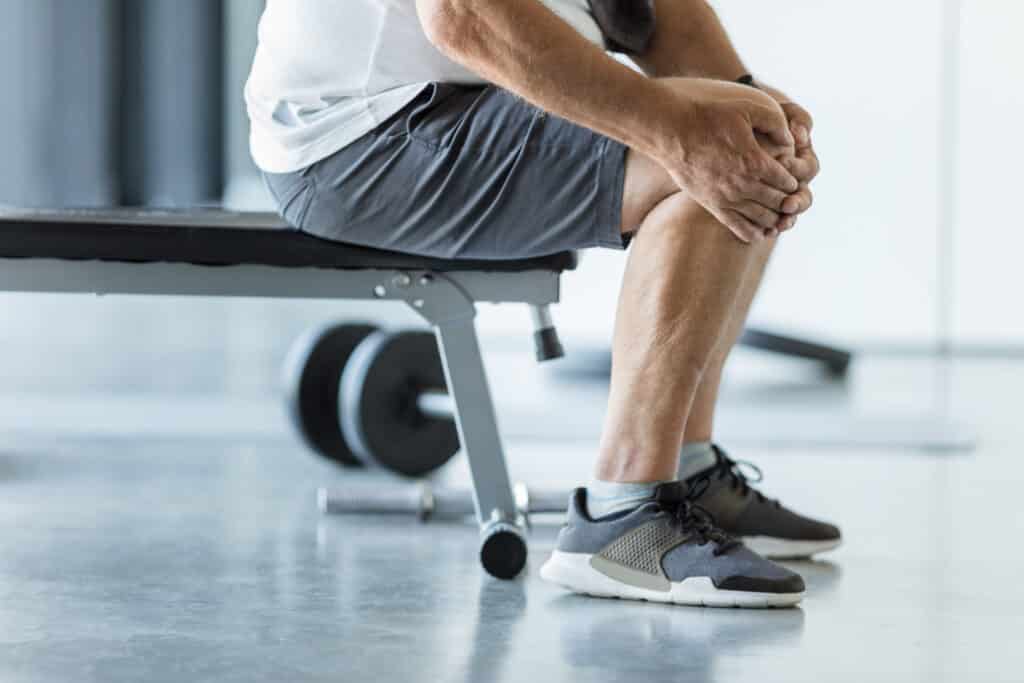 Image of an older man with knee bursitis rubbing his knee at the gym