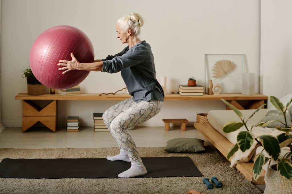 Knee pain while squatting: An older woman doing a squat with an exercise ball.