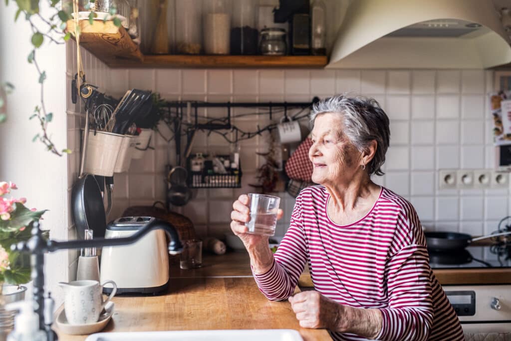 A senior woman enjoys a glass of water during her morning routine in her kitchen