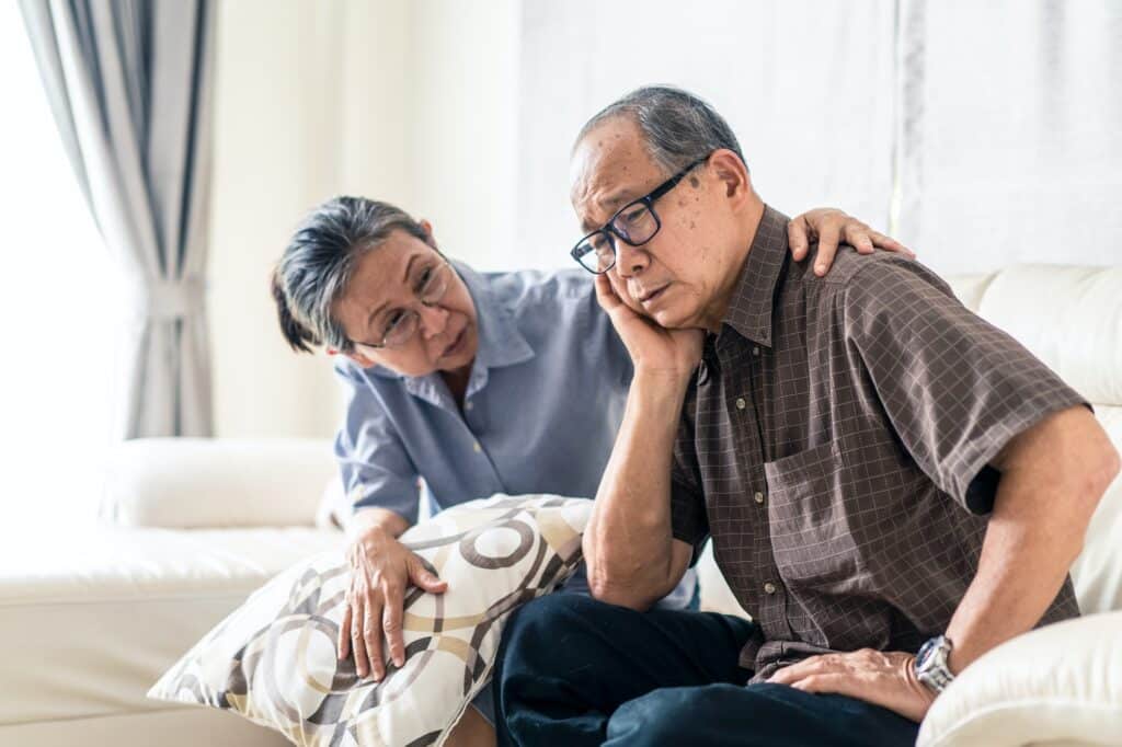 Asian senior old man having headache stress problem put hand on temple sitting on sofa