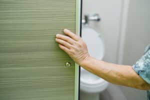 Image an elderly woman's hand on the bathroom door as she copes with urinary incontinence