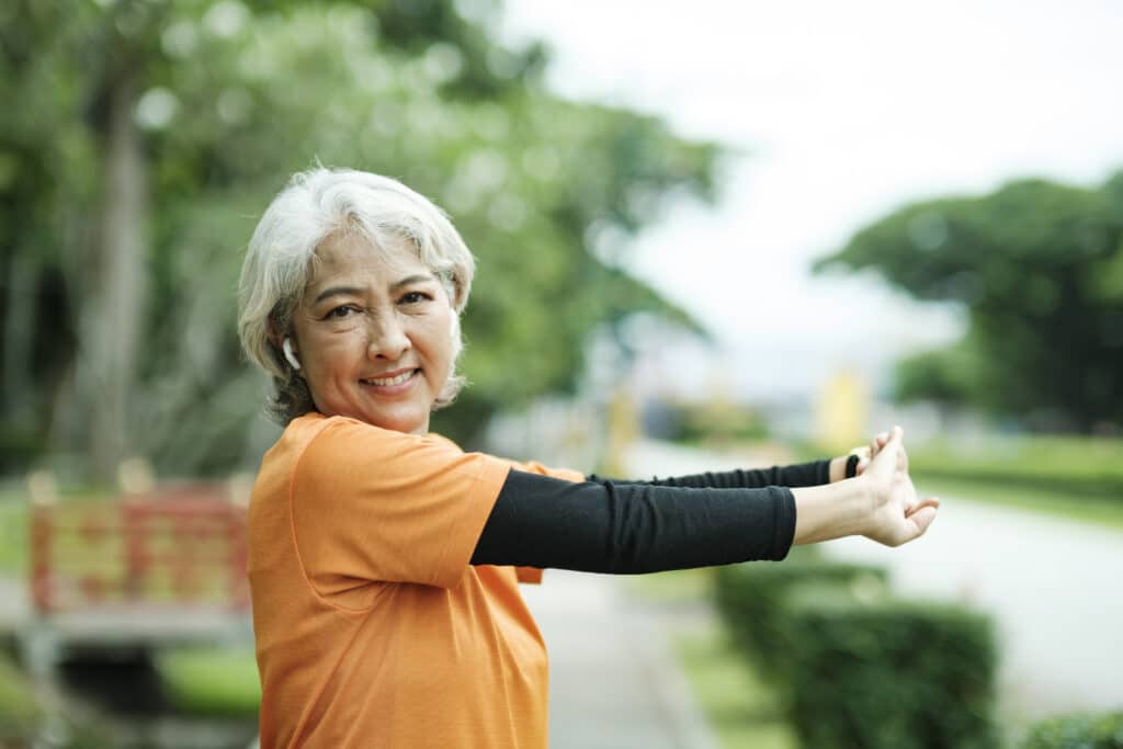 Image of a senior woman stretching her arms and shoulders before a run.