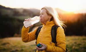 Image of an older blonde woman drinking water while hiking