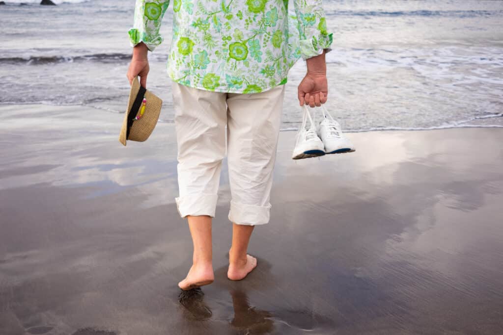 Image a barefoot senior man walking on the beach without hell pain while on vacation.
 
