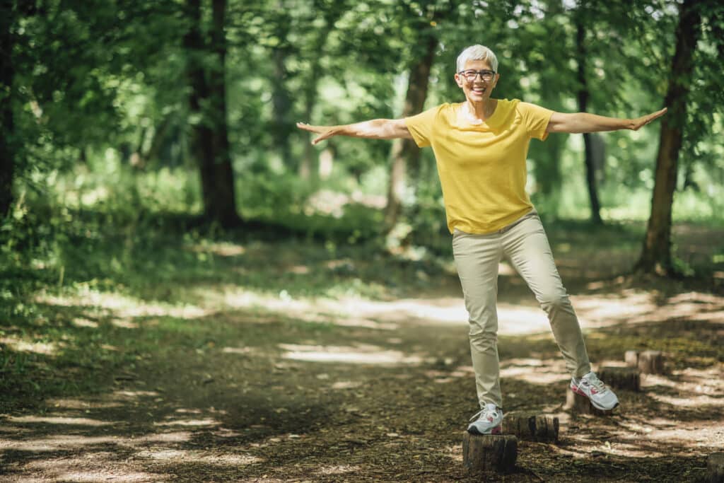 Hearing and balance.  A senior woman balances outdoors on a tree stump