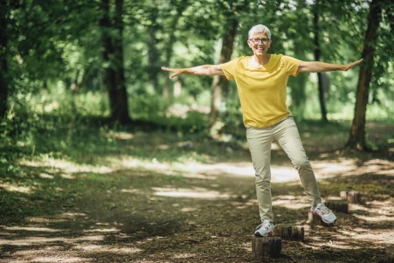 How to do a balance test at home: image of a senior woman balancing on one leg while walking in the woods