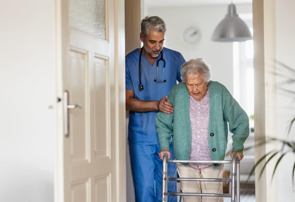 A senior woman with sarcopenia, or age-related muscle weakness being assisted by a nurse as she walks