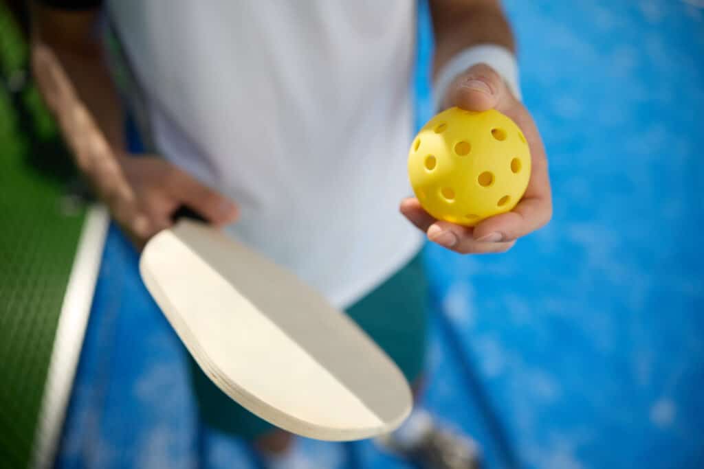 Pickleball vs. Tennis: a closeup image of a man holding a pickleball paddle and ball