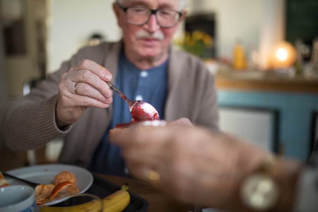 Parkinson's Disease Assistive Tools: Image of a senior man with PD using a spoon at breakfast.