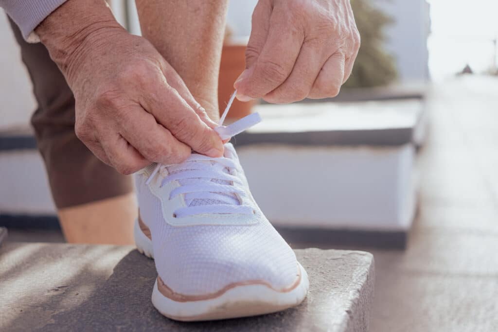 Close-up of woman's hands tying the laces of white sneakers. Caucasian active female sporty fitness runner preparing for jogging outdoors.