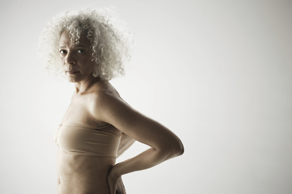 Menopause and joint pain: an image of senior woman with back pain glancing sideways at the camera.