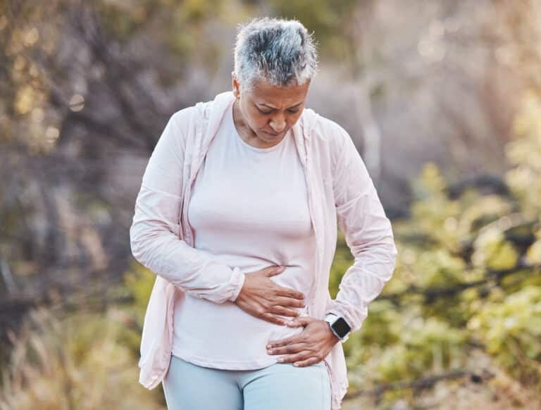Types of Hernia: an older woman rubs a sore spot on her lower abdomen while walking outdoors