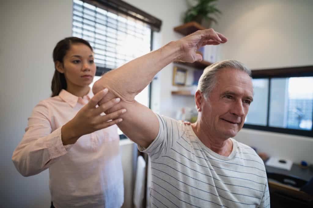 Image of a female physical therapist examining a senior man's shoulder range of motion.