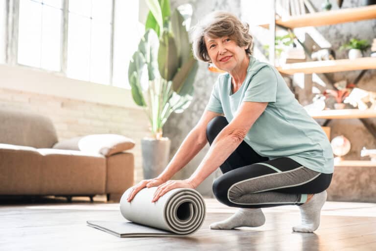 An active senior woman rolls up her yoga mat after doing the dead bug exercise