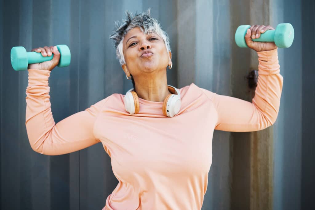 Image of a strong and happy older woman holding weights and making a kissing gesture at the camera.