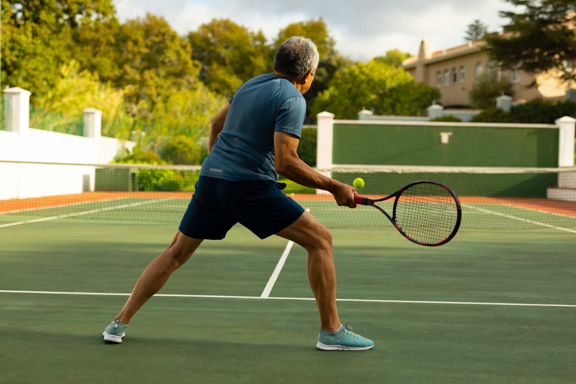 Full length of active biracial senior man holding racket and playing tennis at tennis court