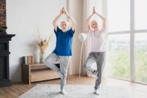 Foot Exercises for Seniors: Grandparents training stretching doing yoga exercises at home on lockdown together keeping balance.