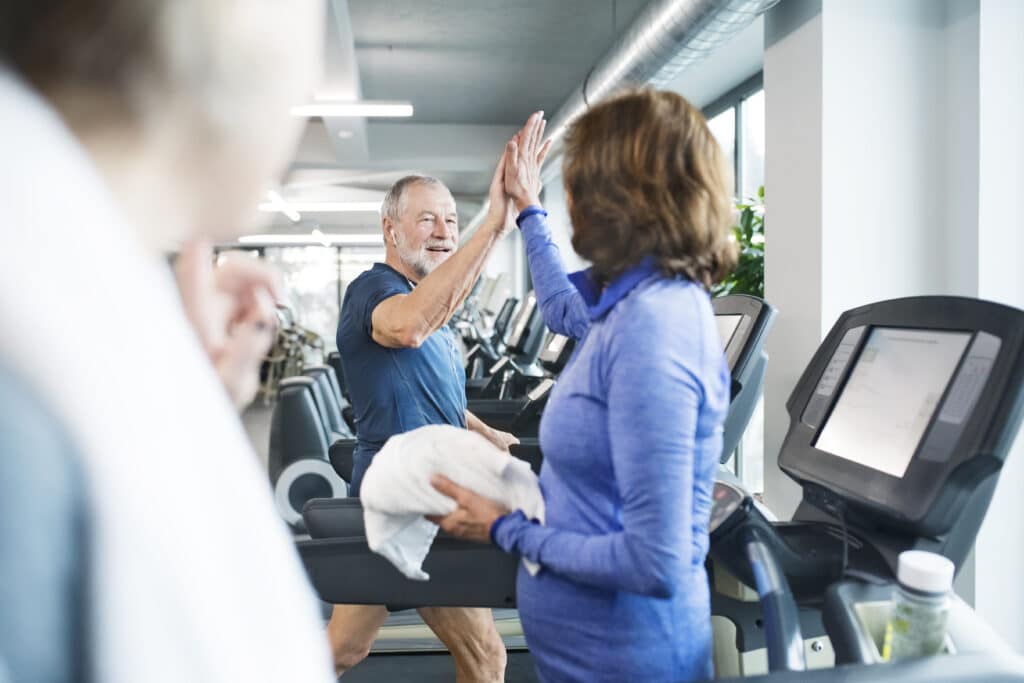 Image of seniors exercising on gym treadmills and high-fiving each other.