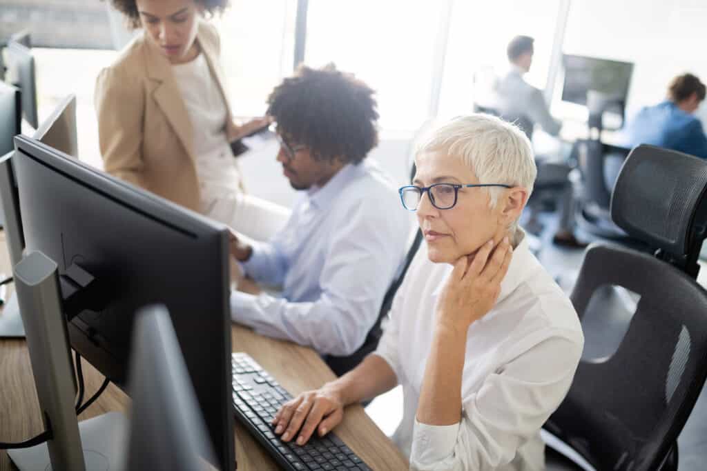 Senior woman seated at computer dealing with neck pain
